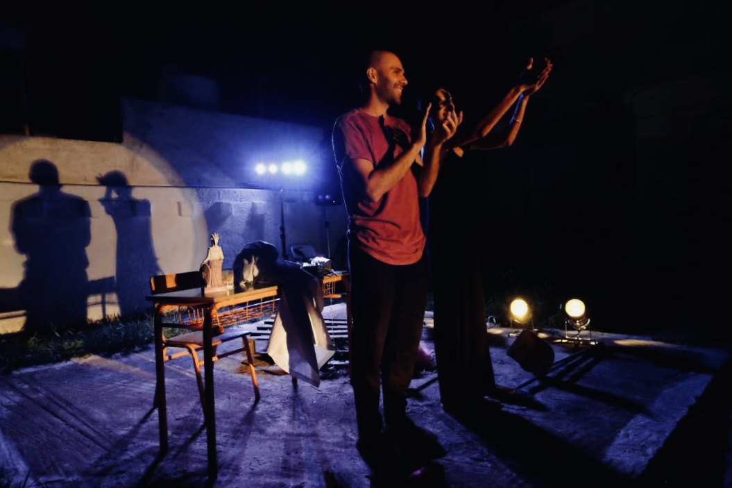 Two performers on the lit courtyard stage during ÉKHO PHONÉ, shadows cast on the museum wall