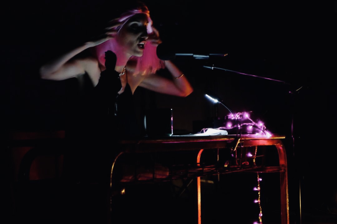 Denia Mimerini at the microphone under pink stage light during ÉKHO PHONÉ