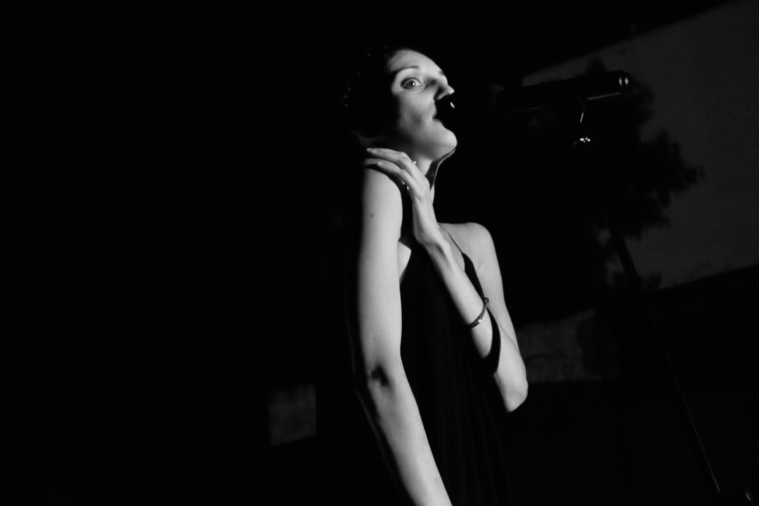 Black and white portrait of Denia Mimerini performing into the microphone